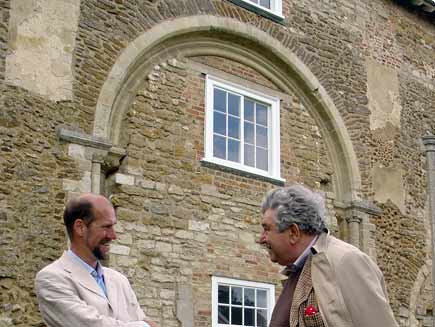 Martin Palmer (left) with Prof Jonathan Riley-Smith in front of the grey stone and brick building of Denny Abbey.  Gaps and repairs are visible all over the wall
