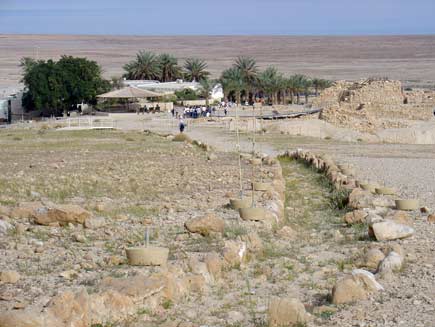 The remains of a stone-walled channel can be seen curving towards a small settlement of buildings surrounded by small stands of desert trees