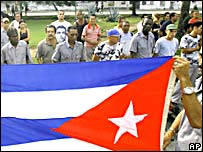 Cubanos cantando hino em frente à bandeira, em Havana