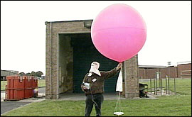 A man  holding the radiosonde.  This is a Hydrogen-filled  balloon about 1 metre across - attached to a cradle in which the sensors and radio transmitter sit