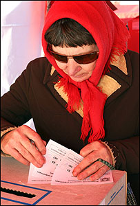 Жінка у червоній хустині з кількома бюлетенями.