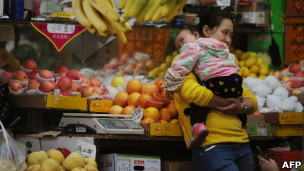 上海一名妇女抱着婴儿走过一处水果摊（9/11/2012）