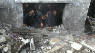 Palestinos em meio aos destroços de uma casa alvejada na Cidade de Gaza, neste domingo (AFP)