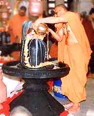 A Hindu monk in orange robes pours water over the phallic symbol of Shiva