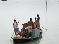 नाव में सामान लादकर ले जाते बाढ़ पीड़ित