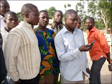 Some of the men of the village crowd around Nicholas as he holds the mobile