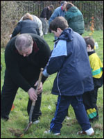 Man helps boy dig hole to plant tree