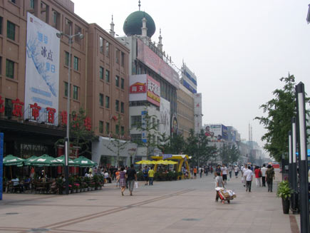 Wangfujing shopping precinct, a wide pedestrian area surrounded by tall buildings.  Shoppers and outdoors café tables are on the pavement