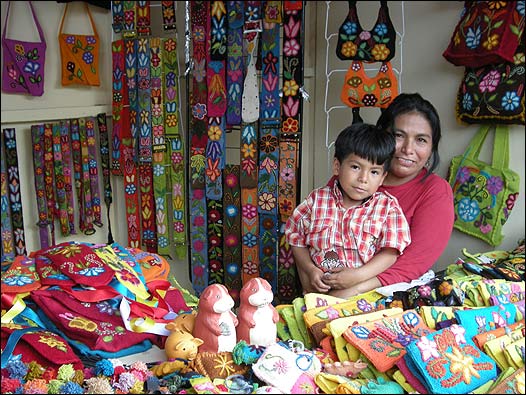 Una señora y su niño frente a su tienda de tejidos y bolsos