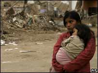 Mulher segura a filha em frente à prédio destruído em Pisco