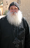 Father Ruwais, smiling Coptic monk in black robe and skull cap with large cross around his neck and a long white beard