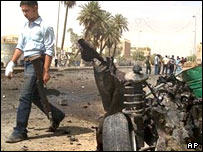 يک پليس مجروح از کنار لاشه خودروی منفجر شده ای در بغداد می گذرد