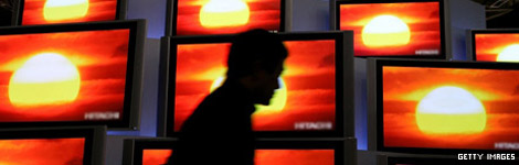 A man walking past televisions in a shop