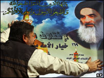 Bir Iraklı, duvara Sistani'nin posterini yapıştırıyor