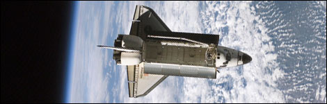 Space shuttle Atlantis, with clouds beneath it, orbits the Earth (Image: NASA)
