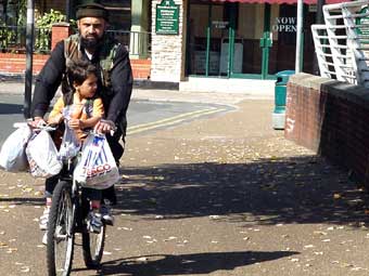 Tad a merch yn mynd ar y beic i nôl y siopa, ger Stadiwm y Mileniwm