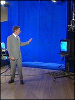 Richard in the studio.  The computer to the left of Richard  generates the charts, and he can see the  composite on the monitor to the right of the  picture