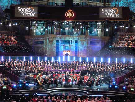 Choirs and orchestra on stage, with the organist visible in an illuminated alcove above the choirs.  The stage, designed on sweeping curved lines, is illuminated with coloured lights in varying patterns