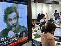TV com a notícia da prisão de Saddam em sala de operações de mercado