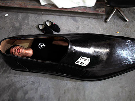 A man lies inside a giant shoe.