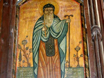 A colourful, ancient painting of Saint Macarius, bearded with halo and religious dress, holding a Christian cross and a two-headed staff