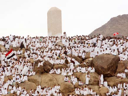 Mountain on the plain of Arafat where dozens of people  dressed in white sit in contemplation and prayer