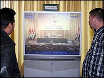 Irak parlamentosunda yapılan oturumu dev ekranlardan izleyen iki kişi