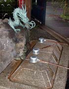 Water trough outside at a shrine, with ladles, a wire cover to keep falling leaves out and a miniature dragon statue above