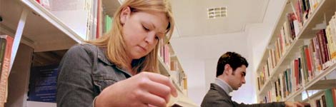 Woman reading a book standing in the aisle between shelves in a library