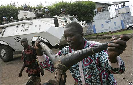 Một người đàn ông mất nhà đẩy chiếc xe đạp gỗ ngang qua xe tuần tra của LHQ