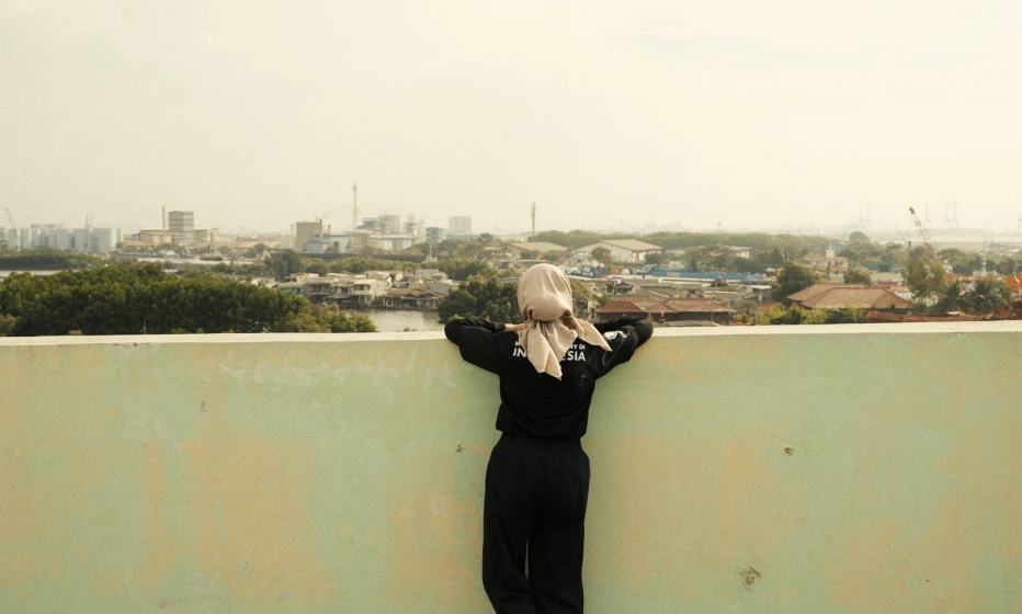A woman with her back to the camera looking out onto a city.